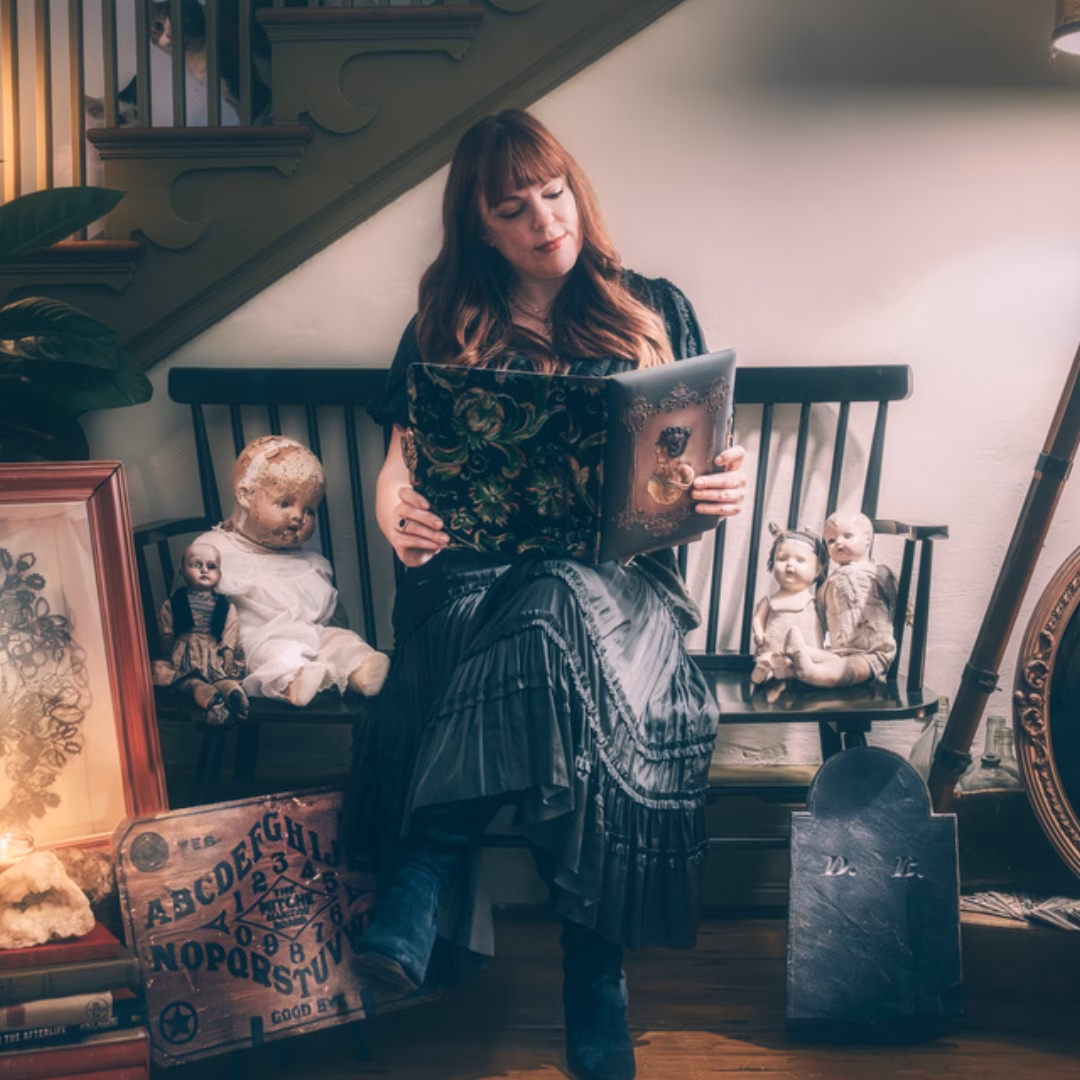 Amy Bruni sitting on a bench reading a book surrounded by haunted artifacts.